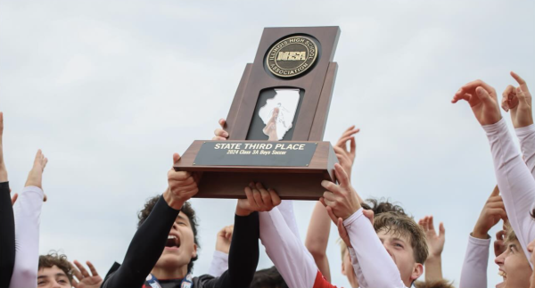 The  varsity boys soccer team holds up their third place trophy.